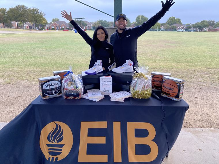 Two EIB teammates behind an EIB-branded table of basketballs and gift baskets at a community giveaway